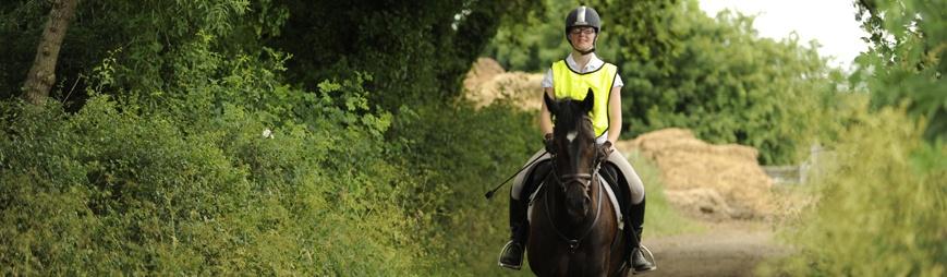 Female student riding horse down a path in a high visibility jacket