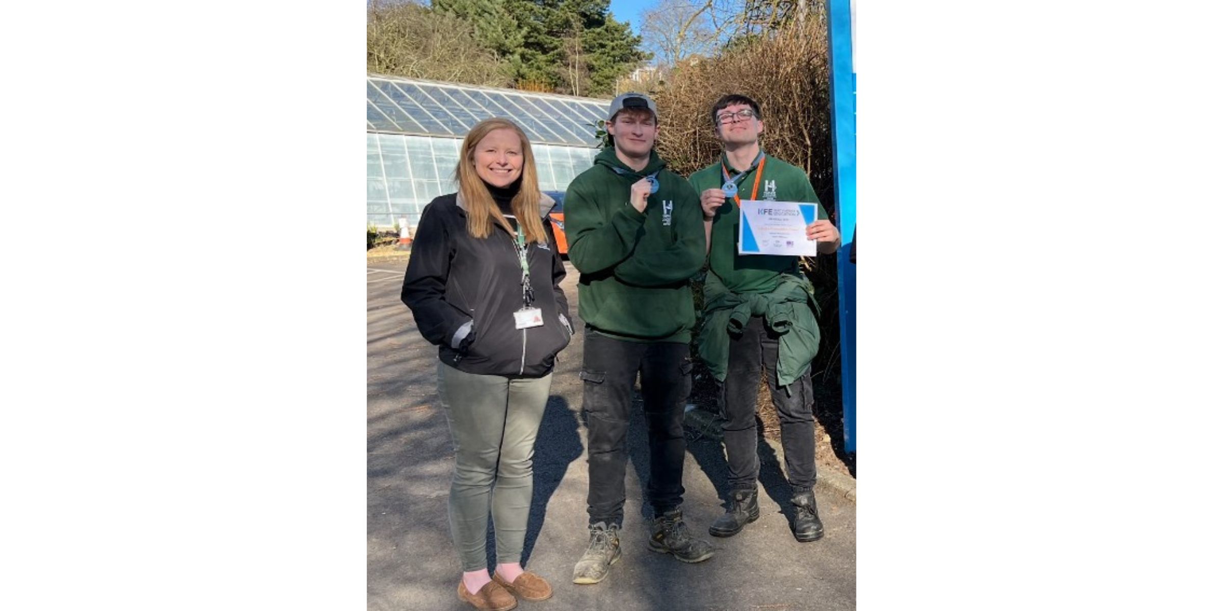 Three adults with glasshouse in background